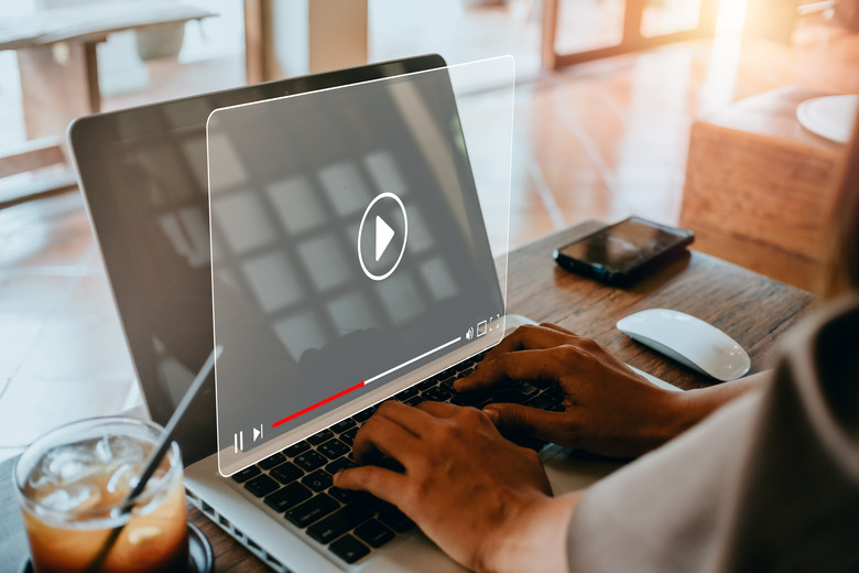 A person is using a laptop to access a video or remote desktop session, with a clear play icon overlay on the screen, representing streaming or remote access functionality.