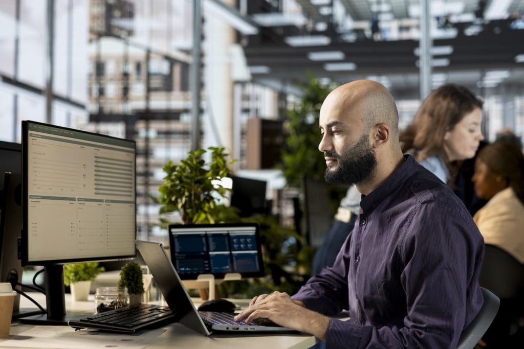 Man working on laptop and desktop computer in a modern office.